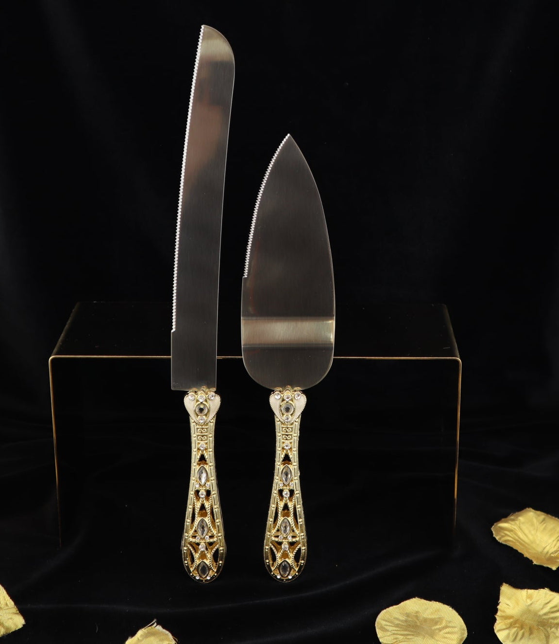 Silver cake knife and server set on a black stand with gold accents against a black background.