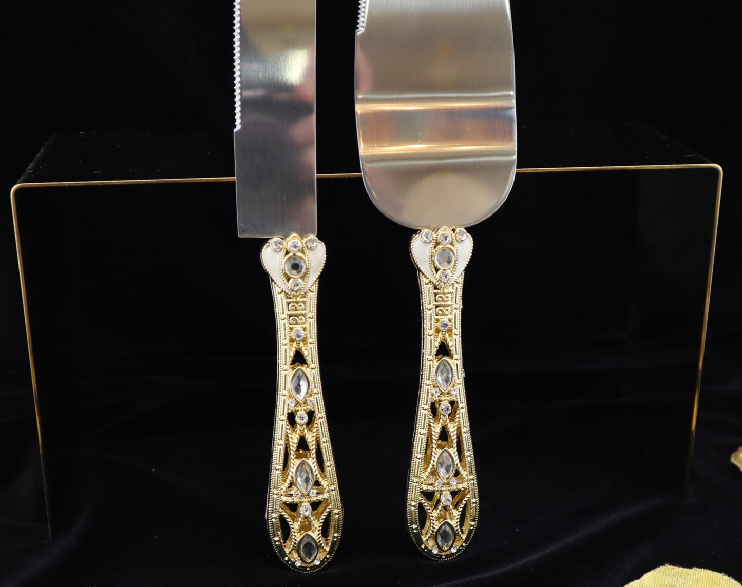 Decorative cake server and knife set with gold filigree design on a black background with gold leaves.