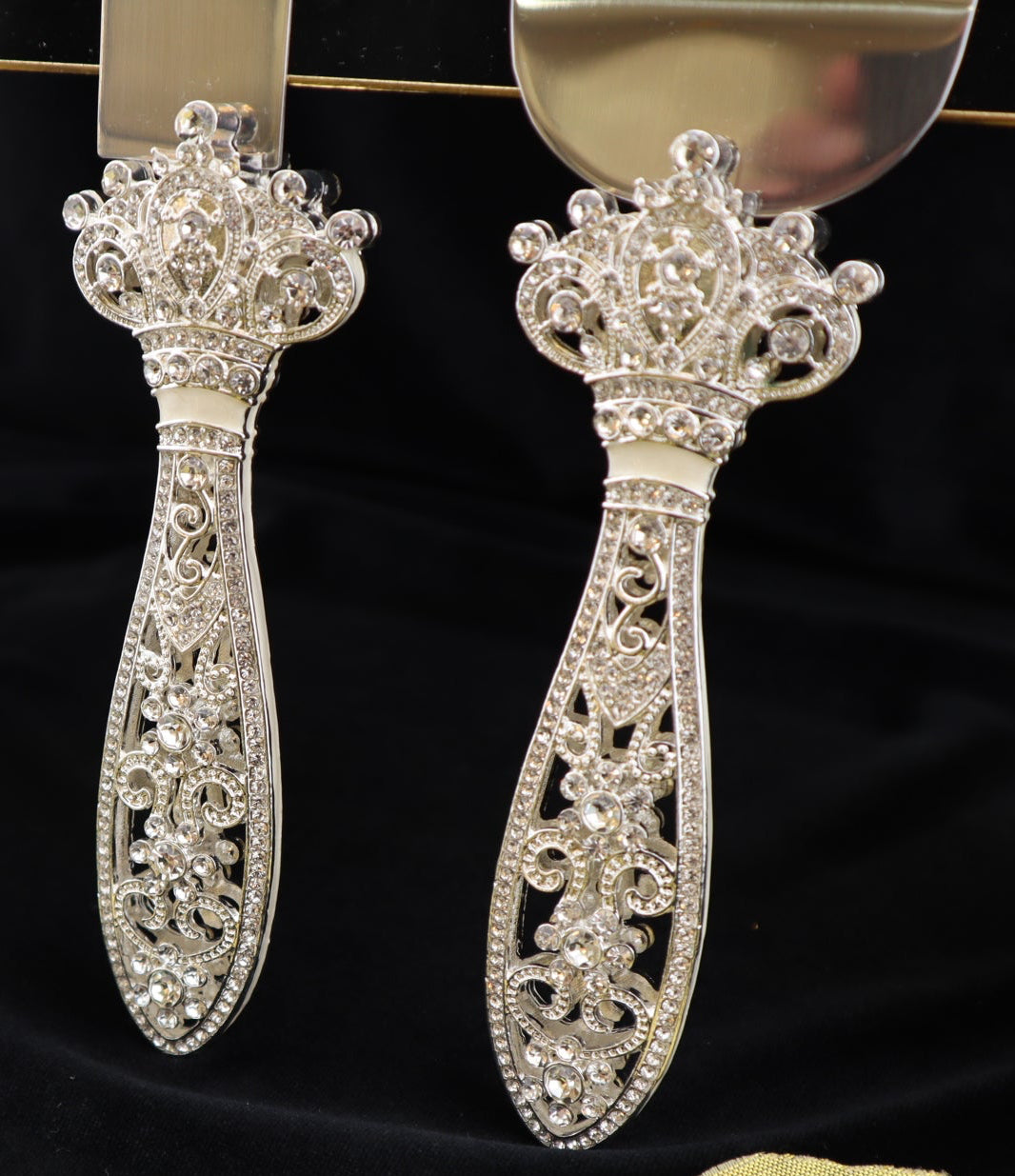 Decorative silver cake server and knife set on a black surface with gold leaves.