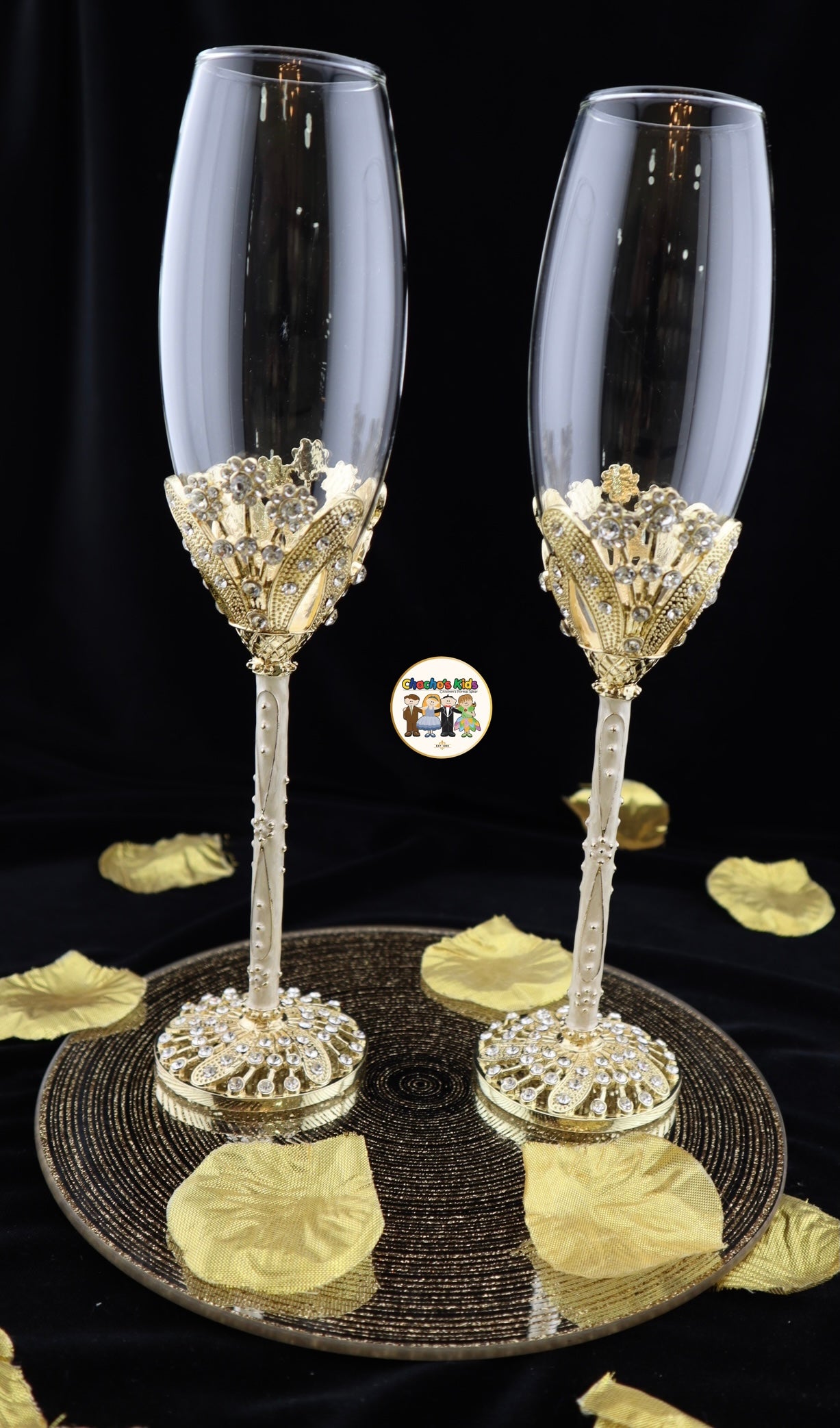 Two elegant Wedding champagne flutes with decorative bases on a black surface with gold leaves.