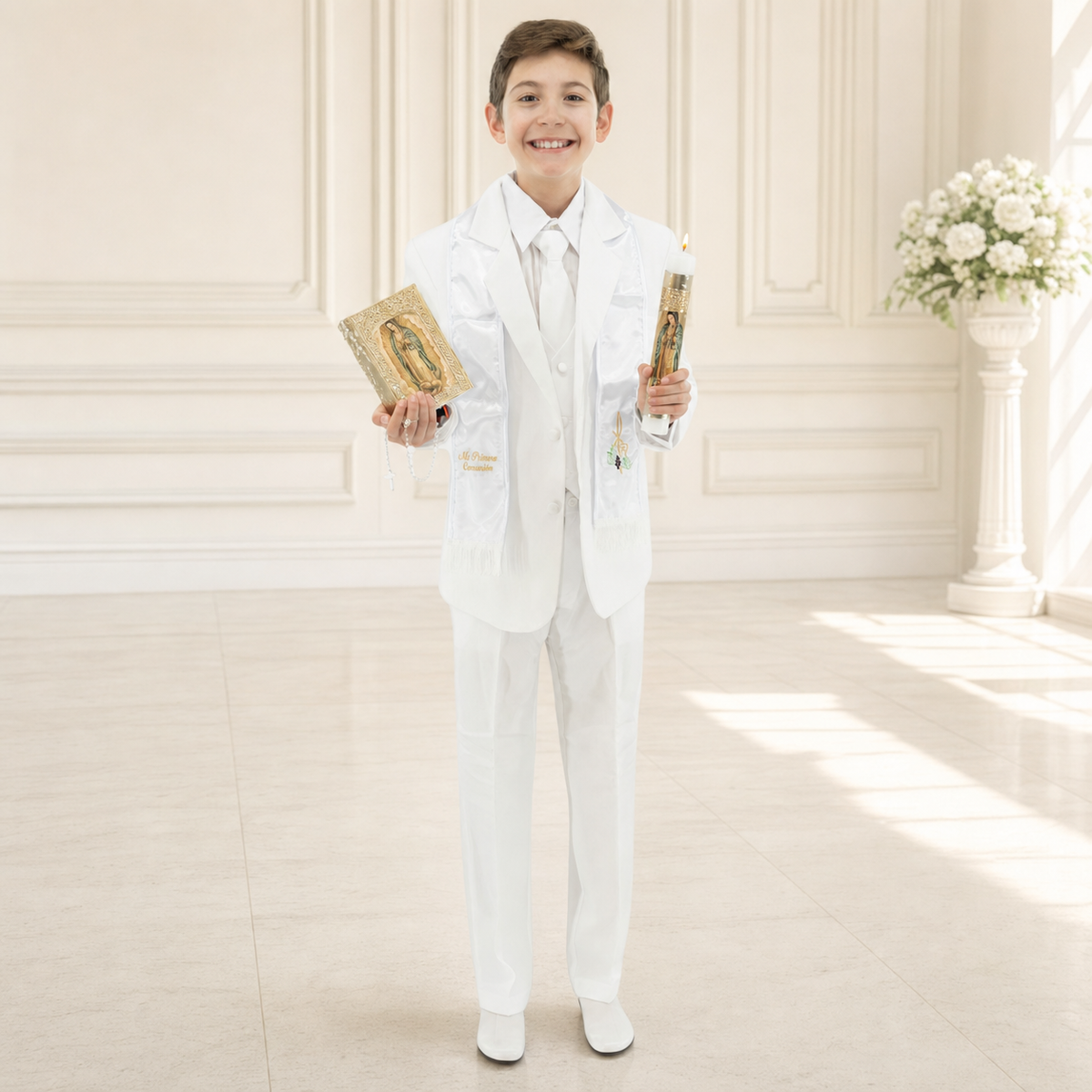 Boy wearing a white First Communion suit, holding a prayer book and decorated candle in an elegant cream interior