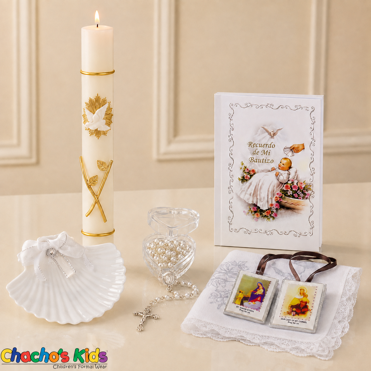 White six-piece Spanish baptism set displayed upright with a lit gold-detailed candle, prayer book, shell, rosary, scapular and lace-edged handkerchief.