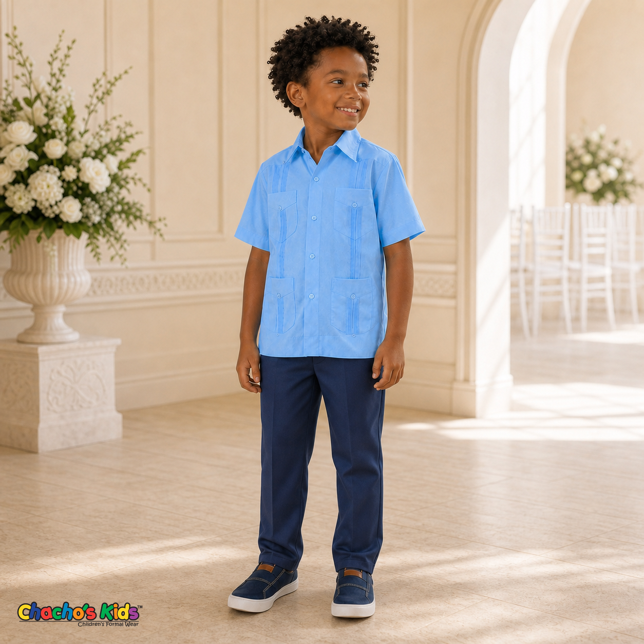 Young boy wearing light blue 100% linen classic guayabera with four pockets and navy dress trousers, full view