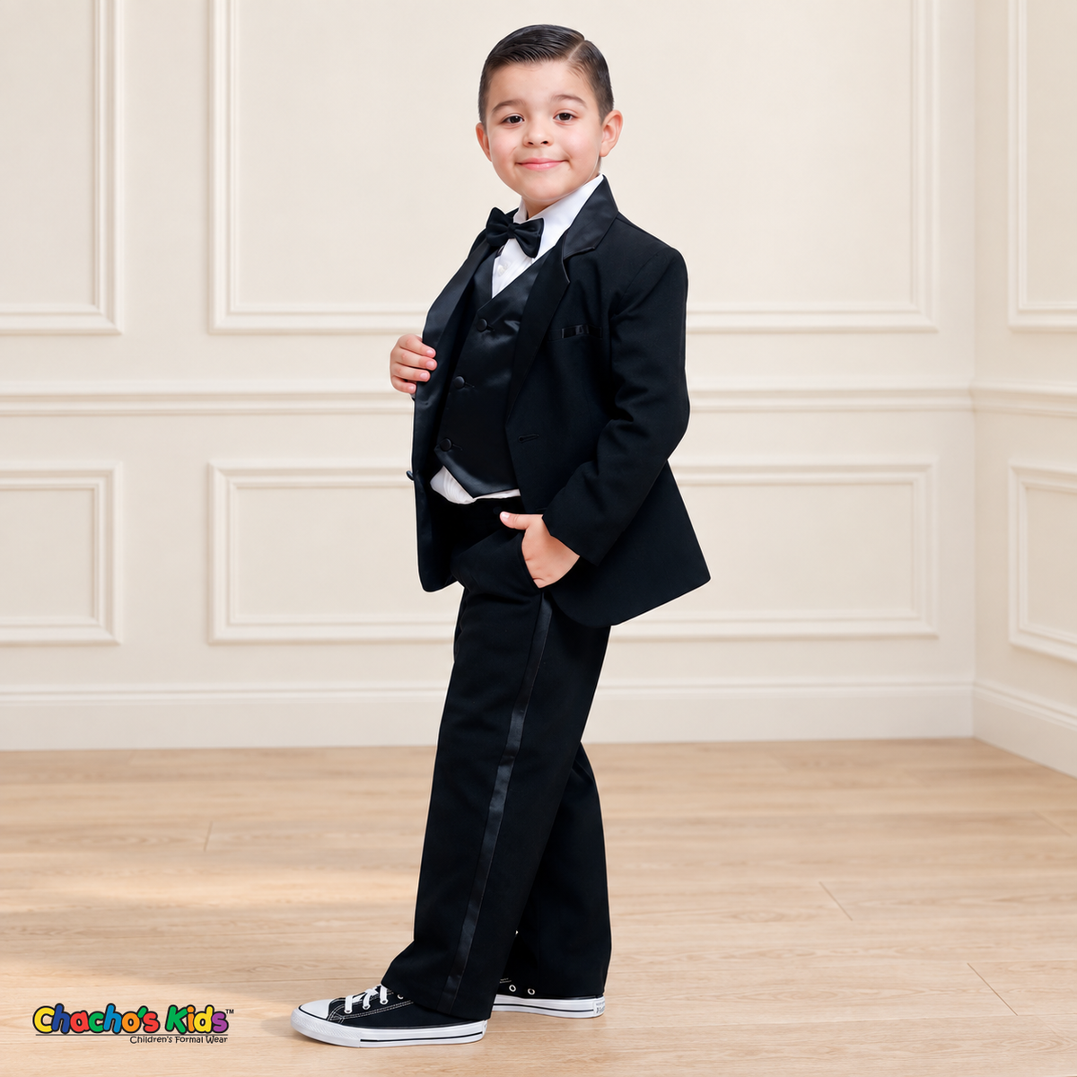 Boys Signature Tuxedo in Black (BY010), child model three-quarter standing view showing the satin vest and trouser side stripe.