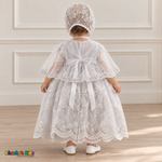 Baby girl wearing a white floral lace baptism dress and matching bonnet, back with cape, showing the ribbon bow and embroidered skirt