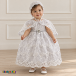 Baby girl wearing a white floral lace baptism dress and matching bonnet, front with cape, showing the jeweled waist and scalloped hem