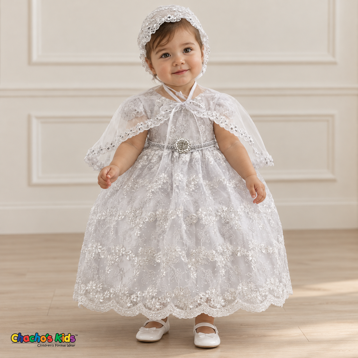 Baby girl wearing a white floral lace baptism dress and matching bonnet, front with cape, showing the jeweled waist and scalloped hem