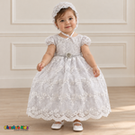 Baby girl wearing a white floral lace baptism dress and matching bonnet, front without cape, showing the jeweled waist and scalloped hem