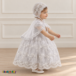 Baby girl wearing a white floral lace baptism dress and matching bonnet, side with cape, showing the embroidered skirt and scalloped trim