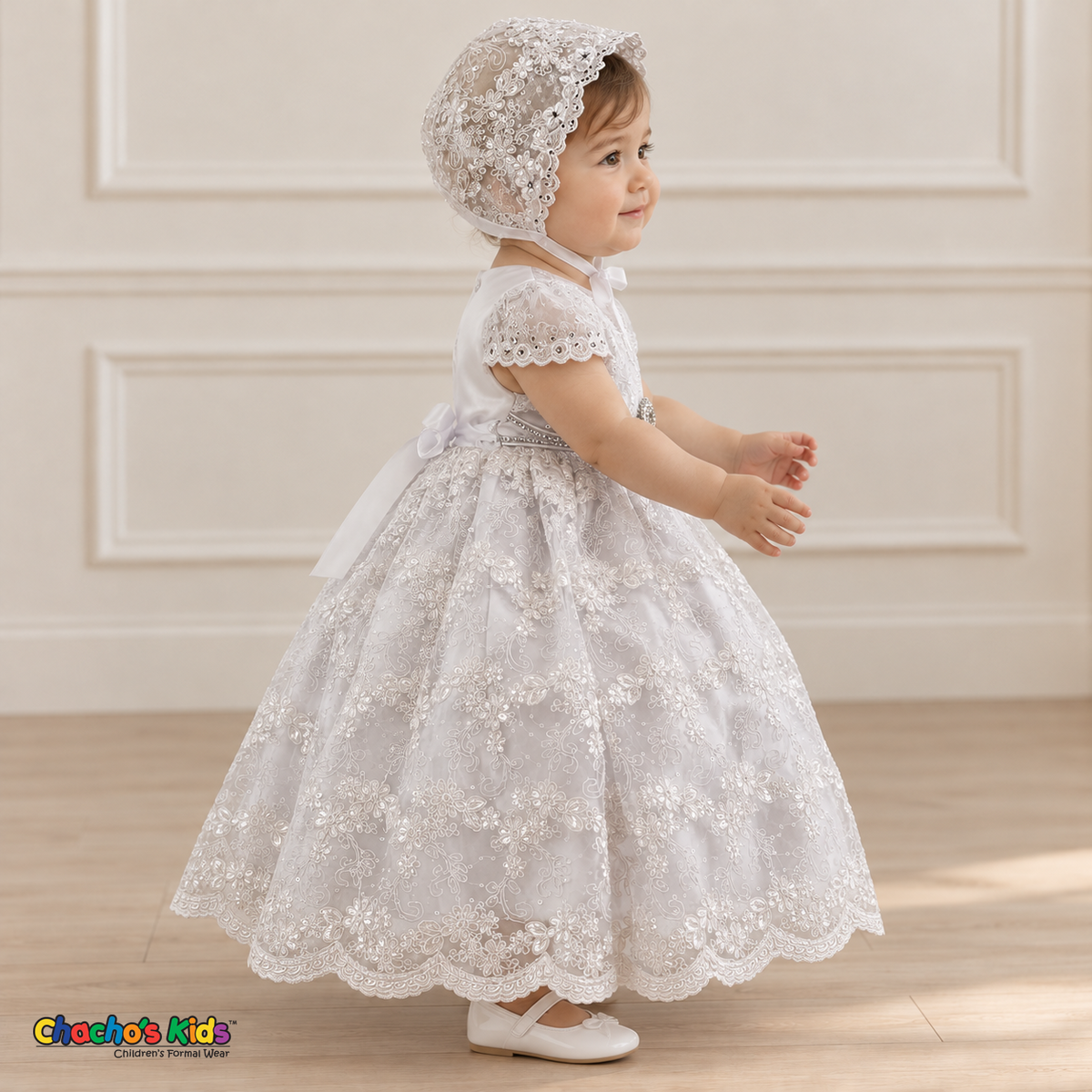 Baby girl wearing a white floral lace baptism dress and matching bonnet, side without cape, showing the embroidered skirt and scalloped trim