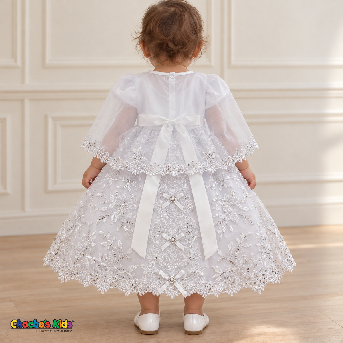 Baby girl wearing the white Virgin Mary Baptism Dress, Style 374, back with cape, showing the satin sash, floral embroidery and ribbon bows.