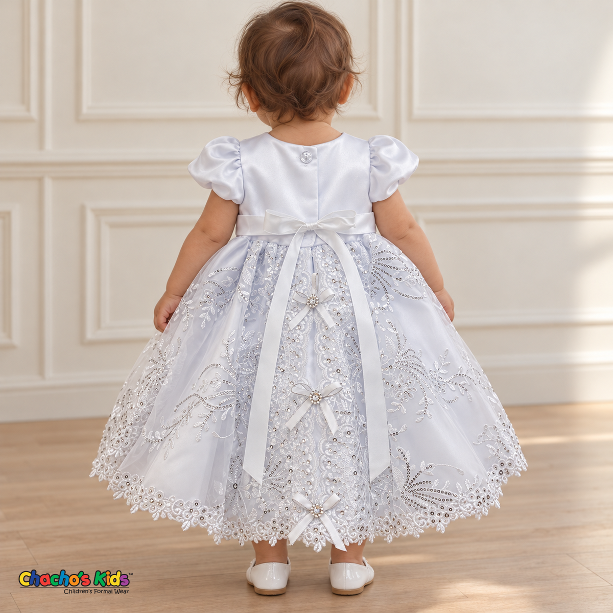 Baby girl wearing the white Virgin Mary Baptism Dress, Style 374, back without cape, showing the satin sash, floral embroidery and ribbon bows.
