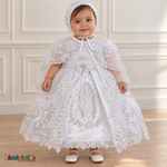 Baby girl wearing the white Virgin Mary Baptism Dress, Style 374, and matching satin bonnet, front view with the sheer embroidered cape, showing silver Virgin Mary embroidery and floral lace.