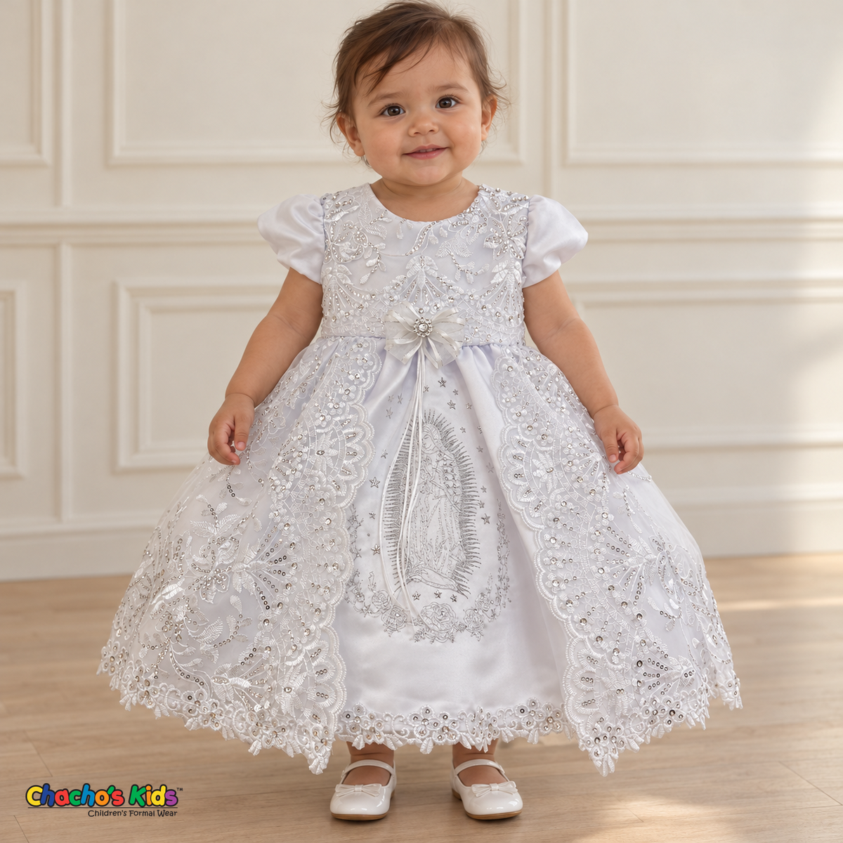 Baby girl wearing the white Virgin Mary Baptism Dress, Style 374, front without cape, showing silver Virgin Mary embroidery and floral lace.