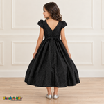 Back view of a girl wearing the black shimmer puff sleeve party dress, Style 444, showing the V-shaped back, zipper and tied sash bow.