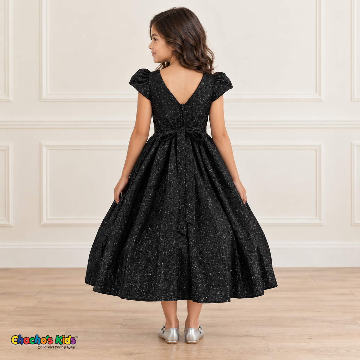 Back view of a girl wearing the black shimmer puff sleeve party dress, Style 444, showing the V-shaped back, zipper and tied sash bow.