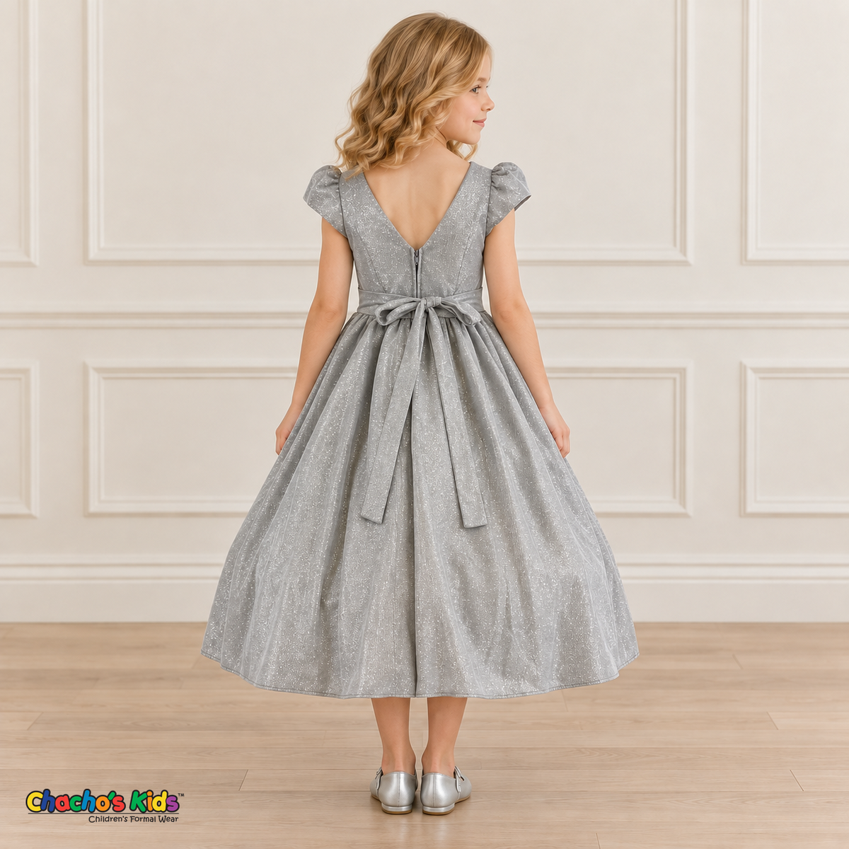 Back view of a girl wearing the silver shimmer puff sleeve party dress, Style 444, showing the V-shaped back, zipper and tied sash bow.