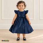 Front view of a baby girl wearing the navy blue Baby Satin Flutter & Bow Dress, Style B263, with flutter sleeves, a rhinestone-center waist bow and a full gathered skirt.