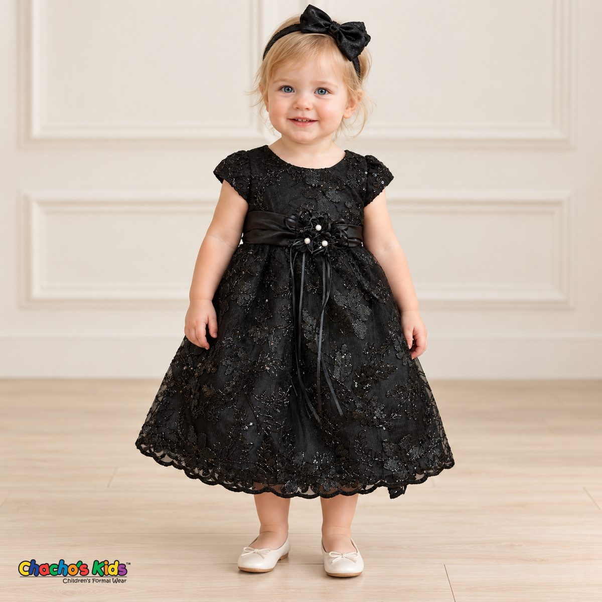 Baby girl wearing the Black Baby Floral Rosette Dress D-1664, front view with matching bow headband.