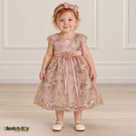 Baby girl wearing the Rose/Gold Baby Floral Rosette Dress D-1664, front view with matching bow headband.