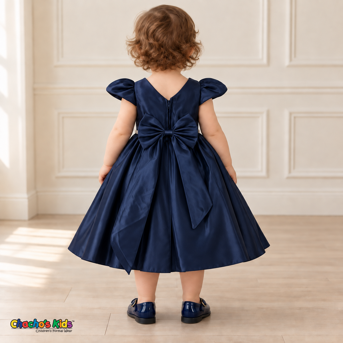 Back view of a baby girl wearing the Navy Blue Baby Satin Puff Sleeve Party Dress (B266), showing the V-shaped neckline, back zipper and large satin bow with two flowing tails.