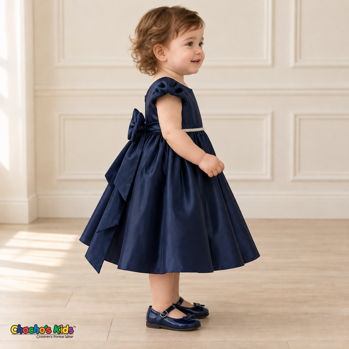 Side view of a baby girl wearing the Navy Blue Baby Satin Puff Sleeve Party Dress (B266), showing the puff sleeve, full skirt and long back-bow tails.