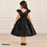 Back view of a girl wearing a black satin party dress with a V-shaped neckline, zipper and large matching satin bow.