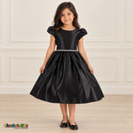 Girl wearing a black satin party dress with puff sleeves, a jeweled waist and a full gathered skirt, front view.
