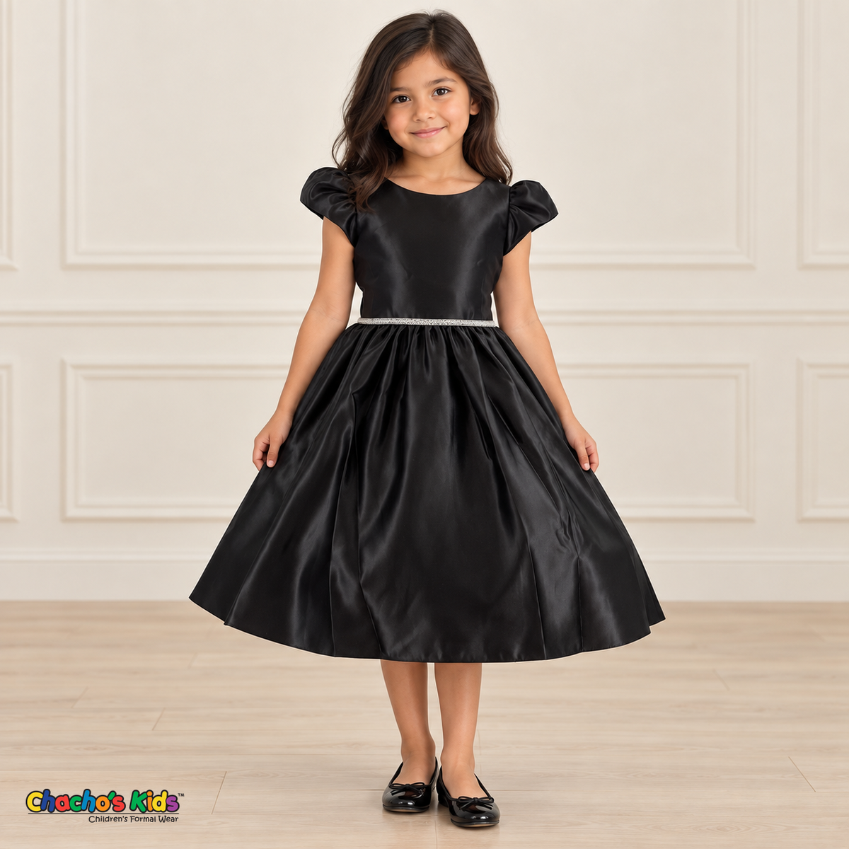 Girl wearing a black satin party dress with puff sleeves, a jeweled waist and a full gathered skirt, front view.