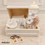 Open white lace baptism chest with champagne floral candle lit and scapular displayed outside.