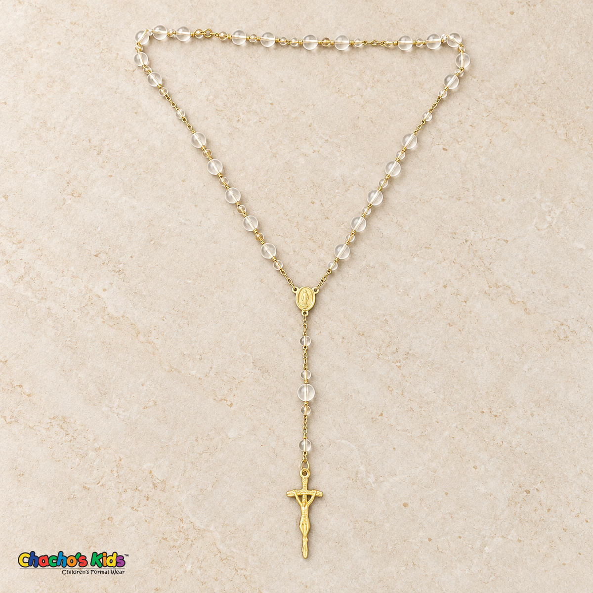 Clear-bead baptism rosary outside its jar with a gold-tone chain, devotional medallion, and crucifix.