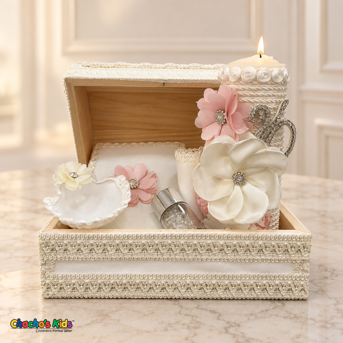 Open long ivory lace baptism keepsake chest with a lit floral candle, pink-flower Bible, ivory shell, handkerchief and rosary jar.