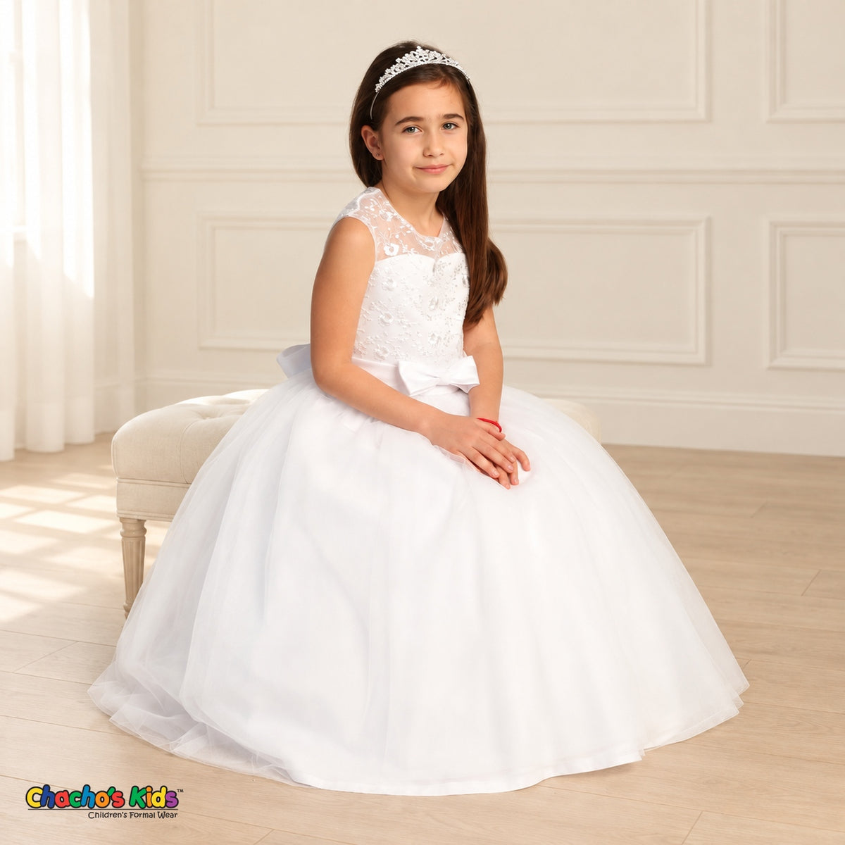 White KE07 floral embroidered tulle dress on the existing child model, seated three-quarter view showing the embroidered bodice and layered tulle skirt.
