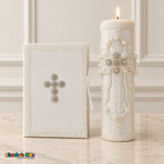 Lit ivory and white baptism candle with pearl and crystal cross beside a Bible with a silver-tone crystal cross.
