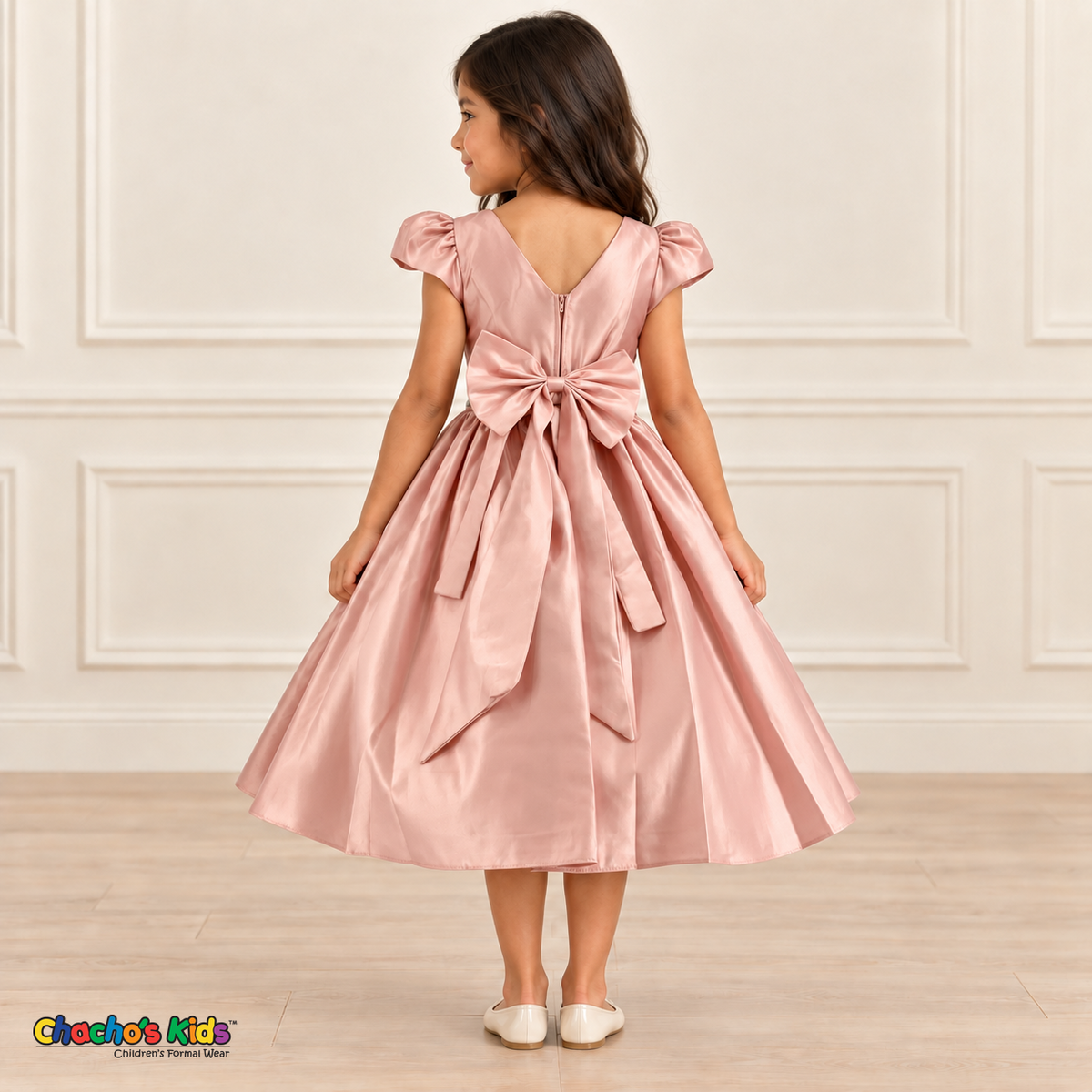 Back view of a girl wearing a soft pink satin party dress with a V-shaped neckline, zipper and large matching sash bow.