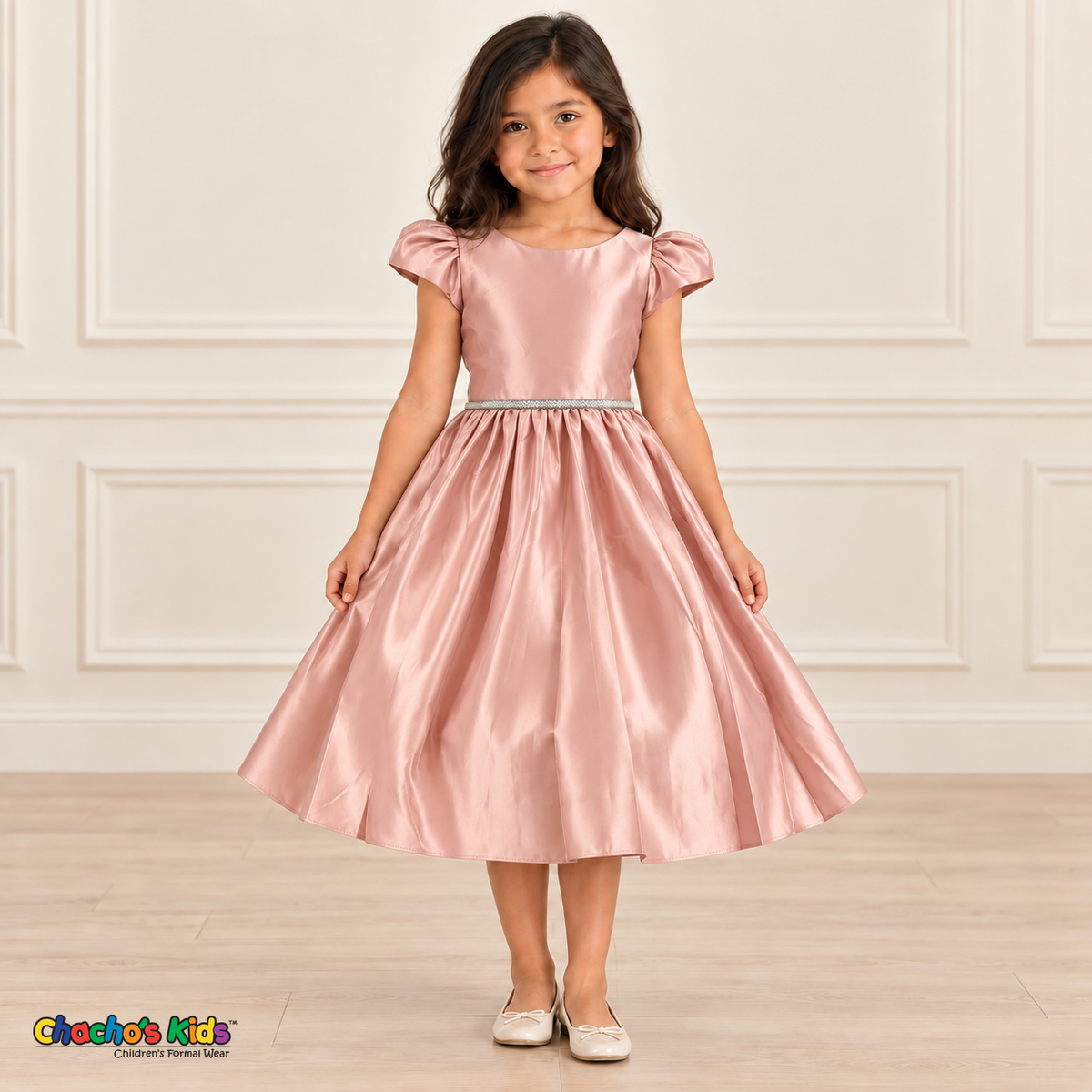 Girl wearing a soft pink satin party dress with short puff sleeves, a sparkling waist and a full gathered skirt.