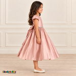 Side view of a girl wearing a soft pink satin party dress with short puff sleeves, a jeweled waist and matching back sash.