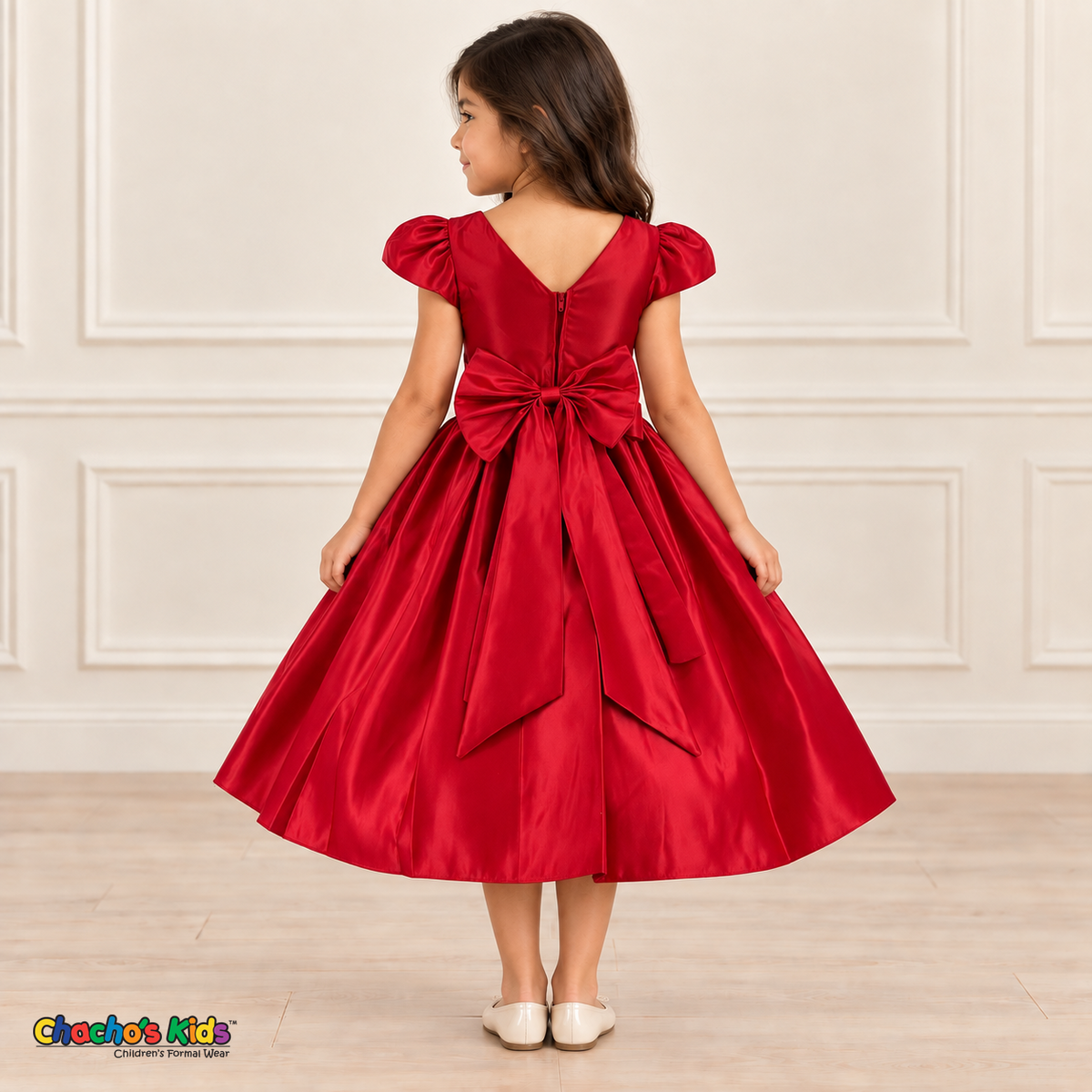 Back view of a girl wearing a red satin party dress with puff sleeves, a V-shaped back and a large matching sash bow.