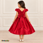 Back view of a girl wearing a red satin party dress with puff sleeves, a V-shaped back and a large matching sash bow.