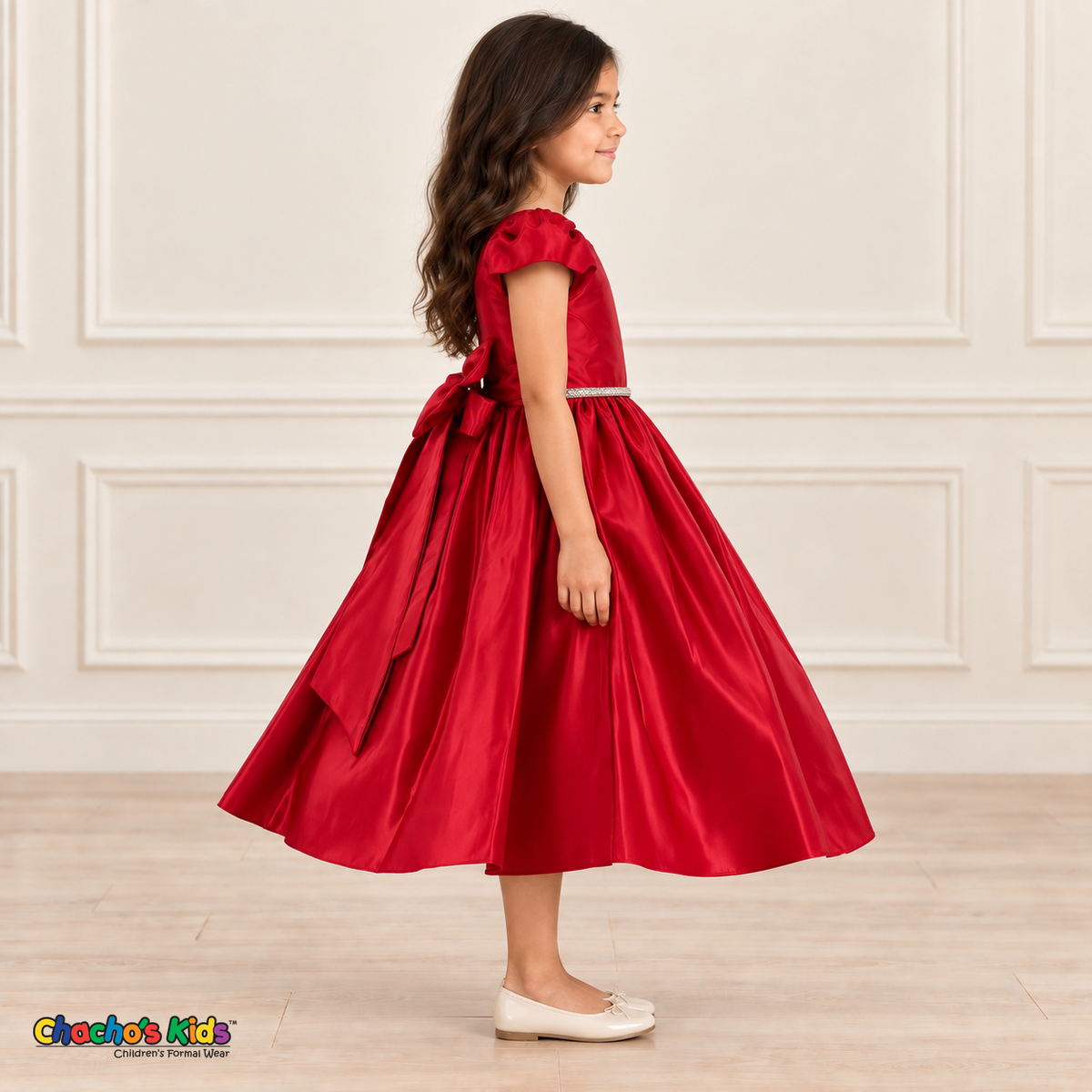 Side view of a girl wearing a red satin party dress with puff sleeves, a jeweled waist and a large back bow.