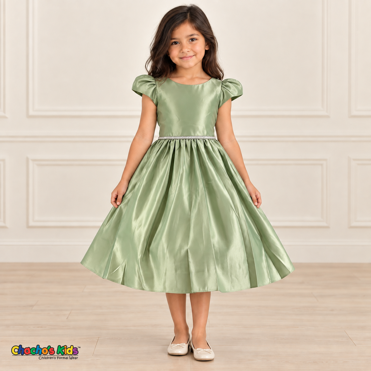 Girl wearing a sage green satin party dress with puff sleeves, a jeweled waist and a full gathered skirt, front view.