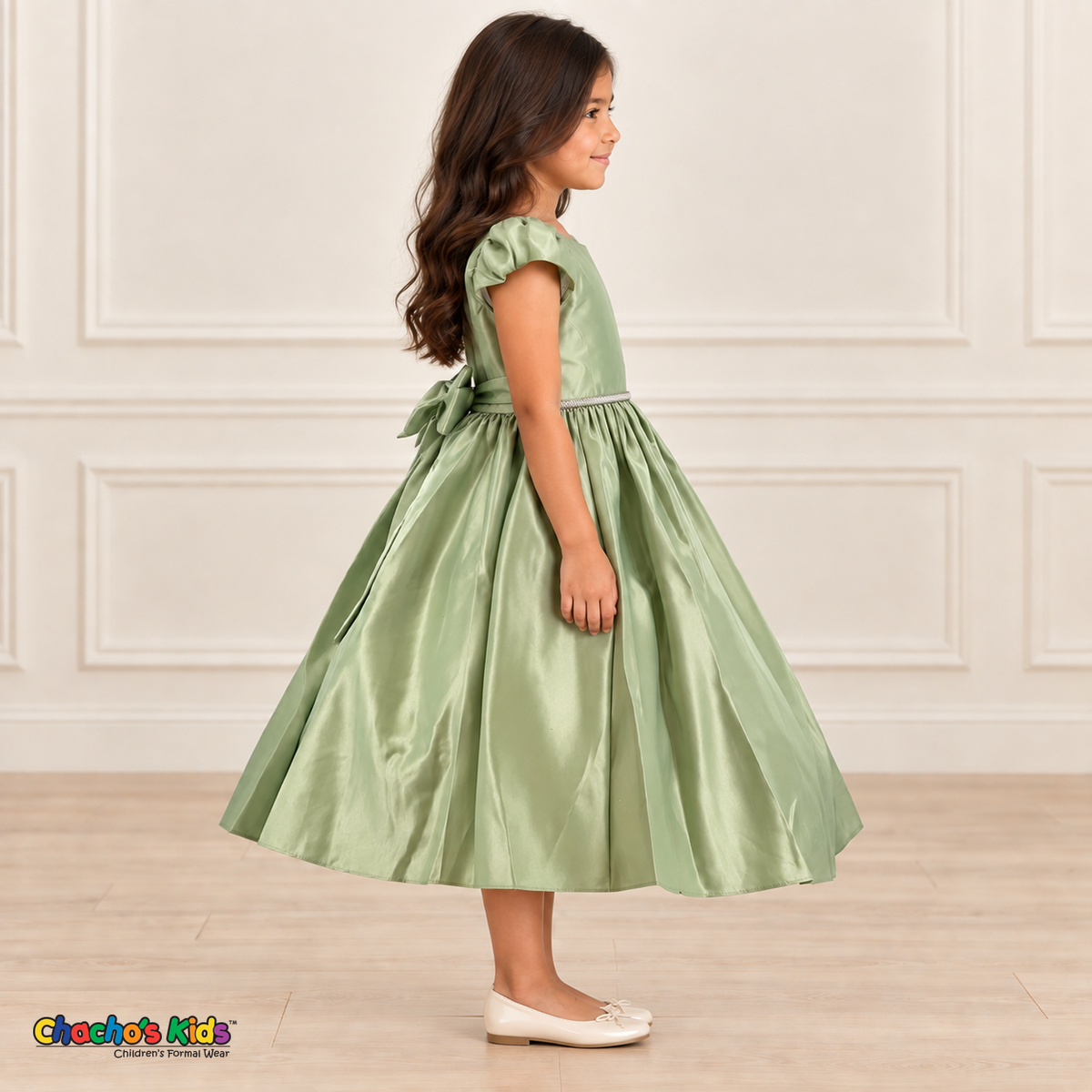 Side view of a girl wearing a sage green satin party dress with puff sleeves, a jeweled waist and a large back bow.