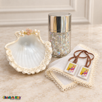Baptism shell with ivory rosette edging, iridescent rosary in a silver-lidded jar, ivory handkerchief, and brown-ribbon devotional scapular.