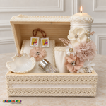Open ivory and peach floral wooden keepsake chest containing a lit baptism candle, Bible, shell, rosary jar, handkerchief, and brown-ribbon scapular.