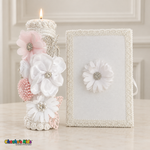 Lit white baptism candle with white and pale pink flowers and sparkling accents beside its coordinating white floral Bible.