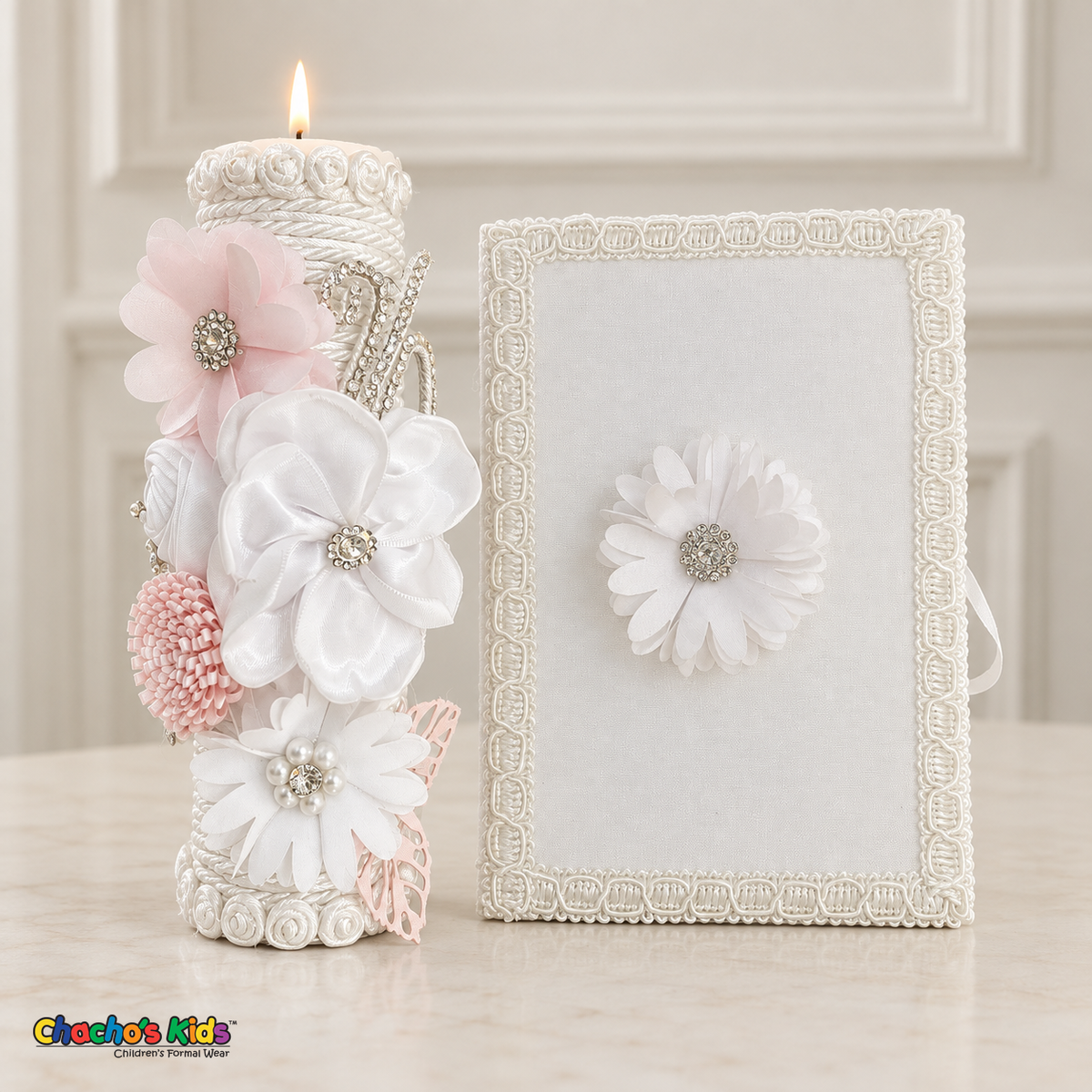 Lit white baptism candle with white and pale pink flowers and sparkling accents beside its coordinating white floral Bible.