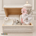 Open white lace baptism keepsake chest with a lit white and pale pink floral candle, floral Bible, shell, and rosary jar.