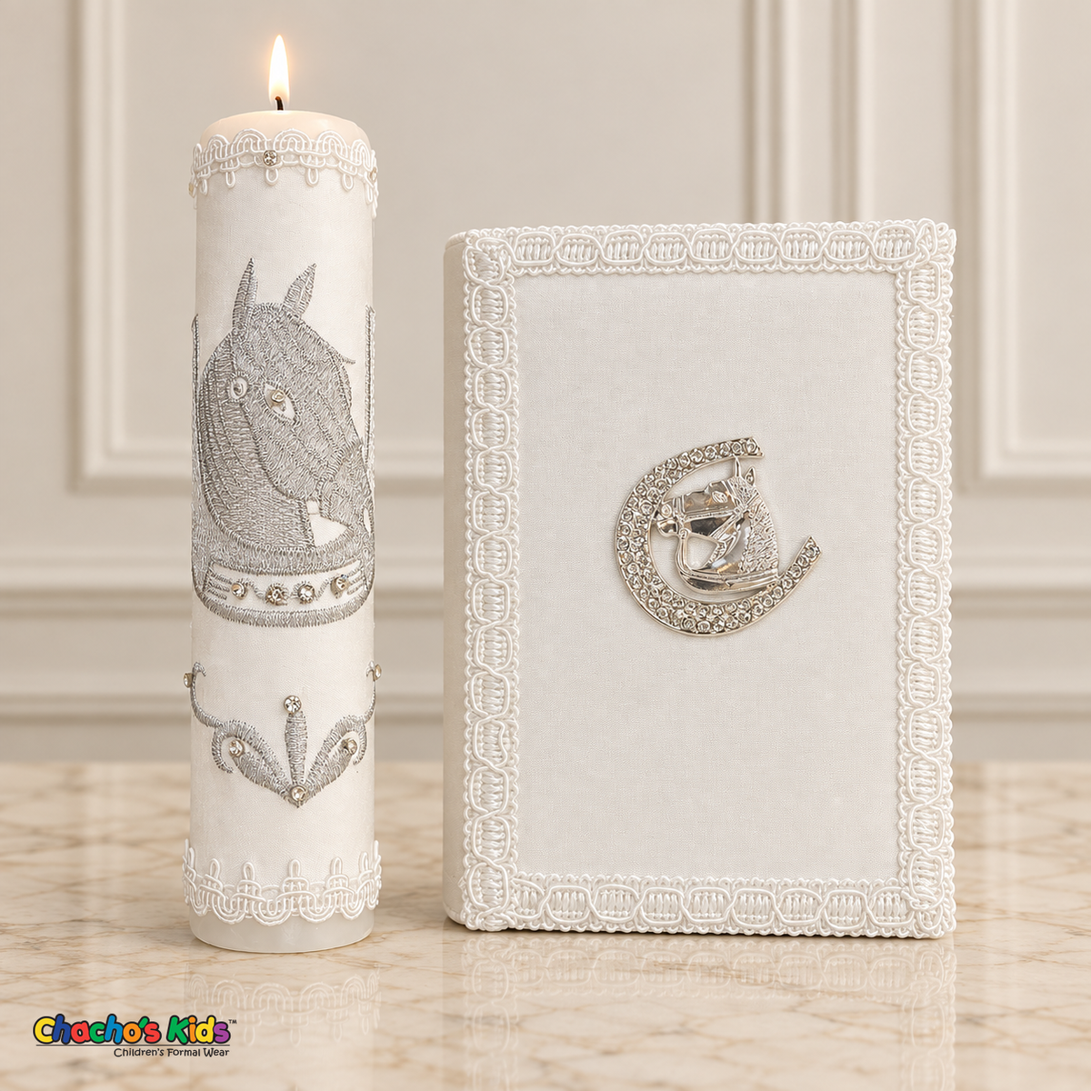 Tall lit white baptism candle with silver horse embroidery beside a white Bible with a silver horse-and-horseshoe emblem.