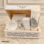 Open white baptism keepsake chest with silver horse embroidery, lit candle, matching Bible, three-rosette shell, white handkerchief and rosary jar.