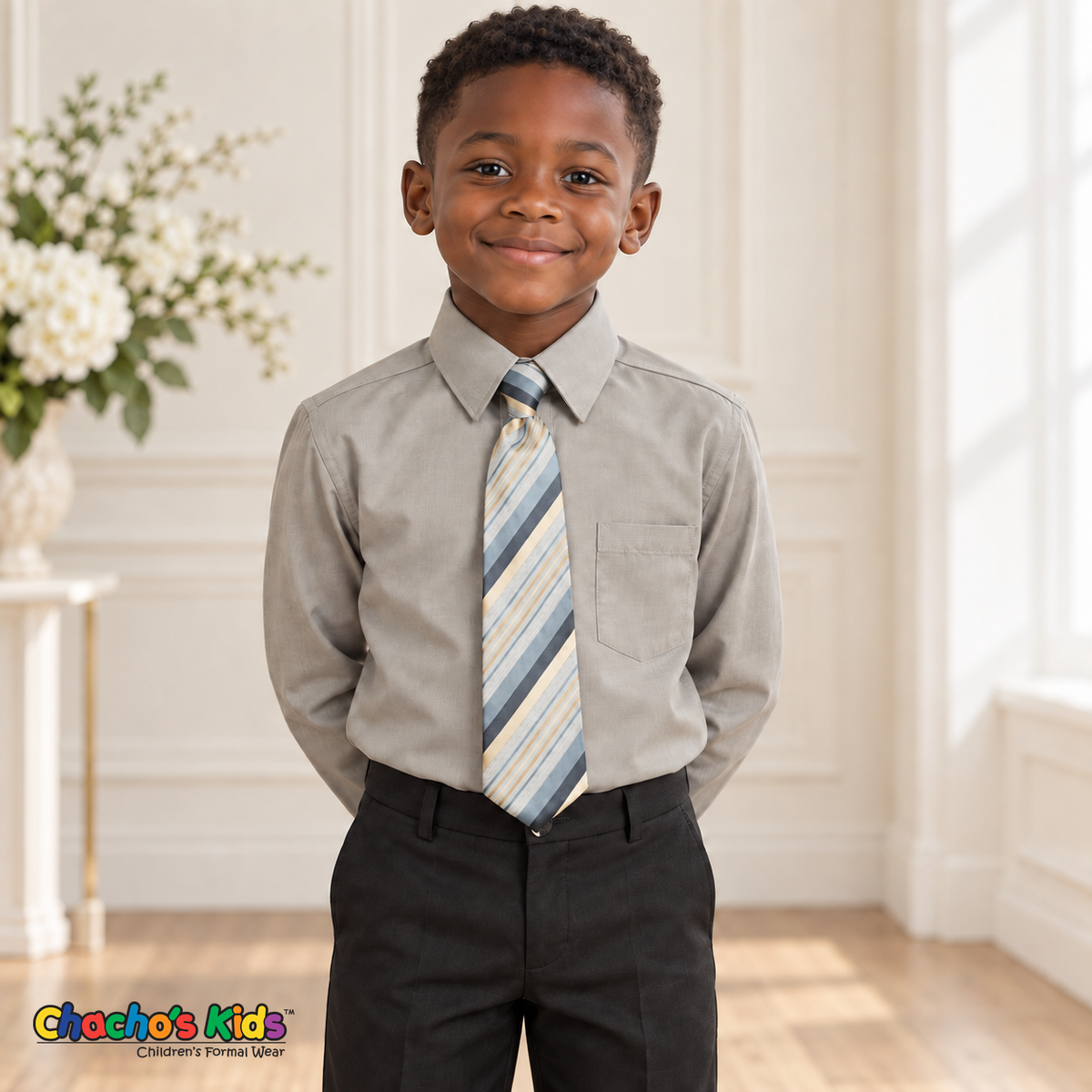 Boy wearing a classic silver long-sleeve dress shirt with its included blue-gray, cream and gold striped tie, tucked into black dress pants
